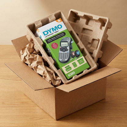 The DYMO LetraTag 100H Plus retail box is shown nestled in protective molded pulp and paper padding within a sturdy brown shipping box, conveying safe and secure delivery.
