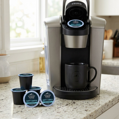 A detailed, close-up photo of several open Kicking Horse Happy Camper K-Cup pods ready to be brewed in a Keurig machine in a home kitchen setting.