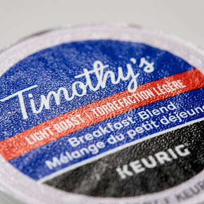 Mentally-precise macro close-up of a Timothy's Breakfast Blend K-Cup pod. The central "Timothy's" script, light roast level, and "Keurig" logo show sharp, high-quality printing on a tactile plastic lid.