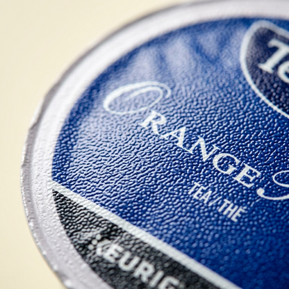 Macro close-up capturing the fine foil texture and precise logo printing of a Tetley Orange Pekoe K-Cup.