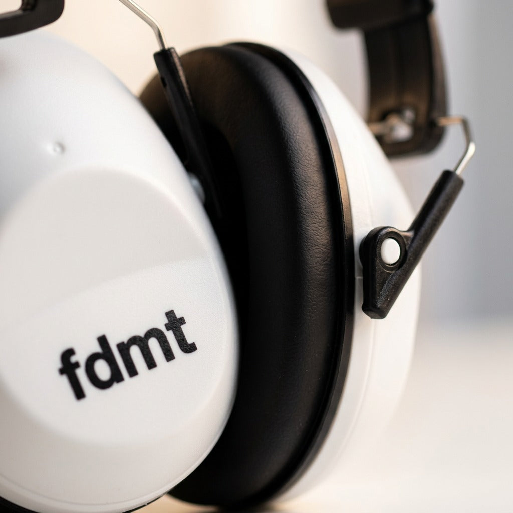 Close-up macro shot of white fdmt protective earmuffs showing the padded black ear cushion and pivot.