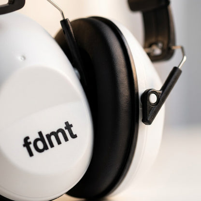 Close-up macro shot of white fdmt protective earmuffs showing the padded black ear cushion and pivot.